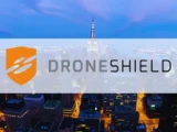 DroneShield-Aktienkurs-Chart mit rotem Abwärtspfeil im März 2026, Hintergrund mit Drohnen und Radarsystemen, Symbol für Kapitalmaßnahme und Partnerschaft