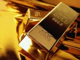Goldbarren und Münzen auf dunklem Hintergrund mit steigendem Preischart – Symbol für sichere Geldanlage 2026