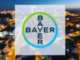 Bayer-Aktie Chart mit leicht steigendem Kurs am 8. April 2026, grüner Pfeil und Hintergrund mit Pharma- und Agrarsymbolen