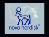 Person hält Smartphone mit Novo Nordisk Logo, im Hintergrund Börsencharts in rot und grün, Symbol für schwankende Aktienentwicklung und Marktdruck.