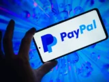 PayPal Logo auf Bildschirm mit Finanzcharts im Hintergrund, Darstellung von Kursbewegungen und Marktvolatilität im Zahlungsdienstleistungssektor.