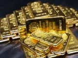 Goldbarren vor fallendem Börsenchart mit Symbolen für Inflation, Ölpreis und US-Dollar-Stärke.