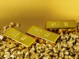 Goldbarren und Goldmünzen mit steigendem Preischart im Hintergrund